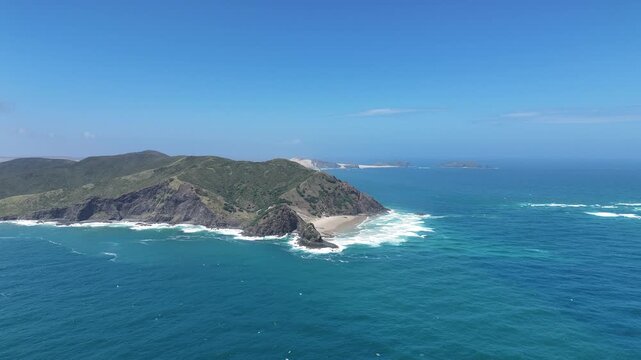 Bright Blue Ocean Waves Crash on Rocky Coast Near an Island in Warm Sunlight With Clear Skies Above, Cape Reinga - New Zealand