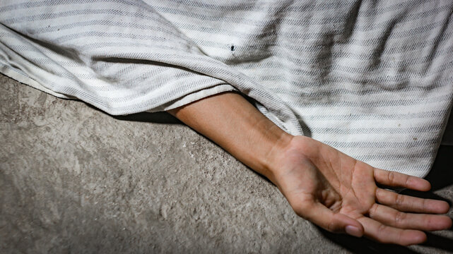 A crime scene concept showing a human hand lying lifeless  or dead body on the concrete floor, with the body covered by a white cloth fabric.murder concept.