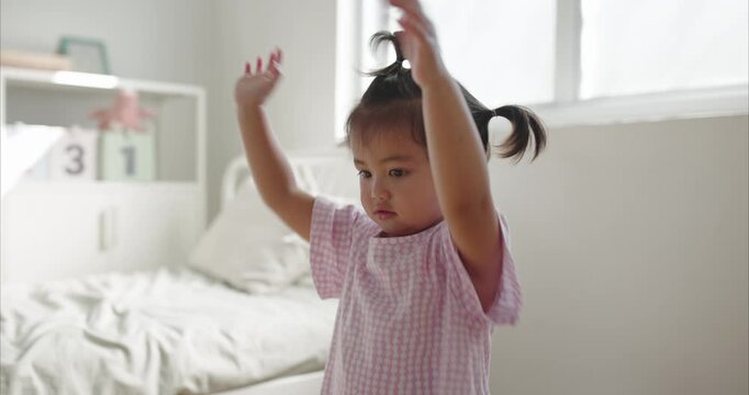 Cheerful Asian little Girl with Pigtails Dance in Cozy Minimalist Bedroom, morning light