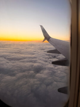 Airplane wing view above clouds at golden sunset from window seat
