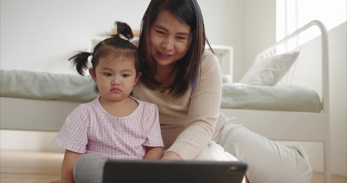 Asian Mother and Two Year Old Toddler Girl Watching Tablet on Floor; Happy Mom and Child Using Digital Device Together