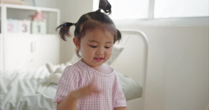 Cheerful Asian little Girl with Pigtails Dance in Cozy Minimalist Bedroom, morning light	