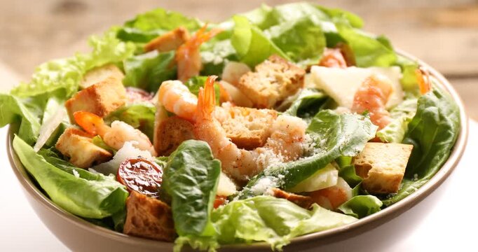 Delicious Caesar salad with shrimps in bowl on table, closeup