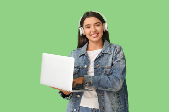 Happy young female programmer in headphones with laptop on green background
