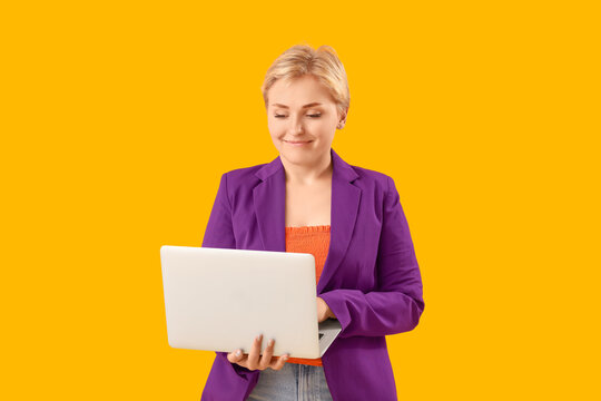 Happy young female programmer with laptop on yellow background