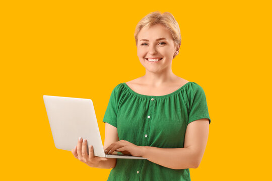 Happy young female programmer with laptop on yellow background