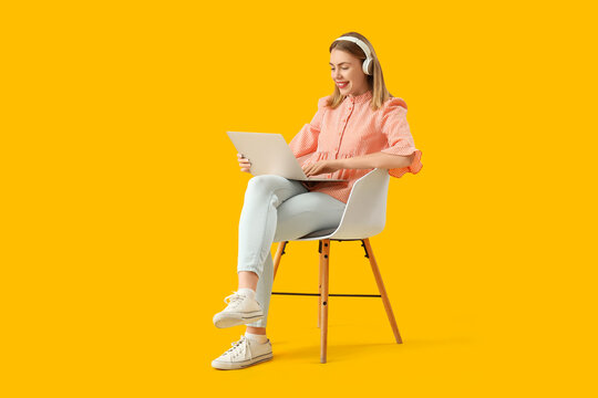 Female programmer with headphones and laptop sitting in chair on yellow background