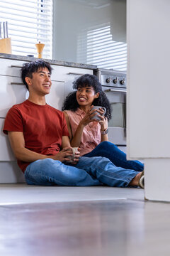 Vertical video: Couple on kitchen floor sipping mugs and causing health icons rising over blinds