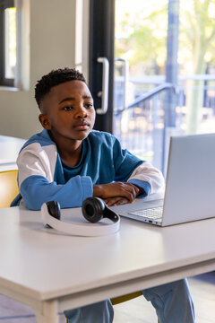 African American child boy wearing blue sweater and pants sitting at desk using laptop, headphones