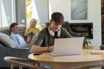 Obraz premium Diverse family using smartphones on sofa as youth male working on laptop at living room table