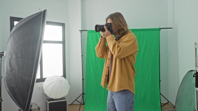 Man checking camera settings while holding the dslr in a studio with green screen and lights; focused creativity.