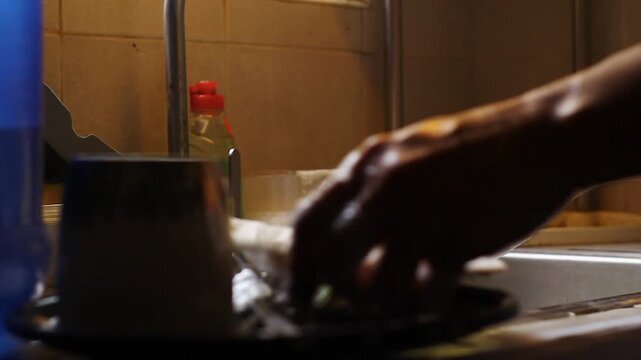 Hand of person washing dishes and utensils with soap and water on the sink.