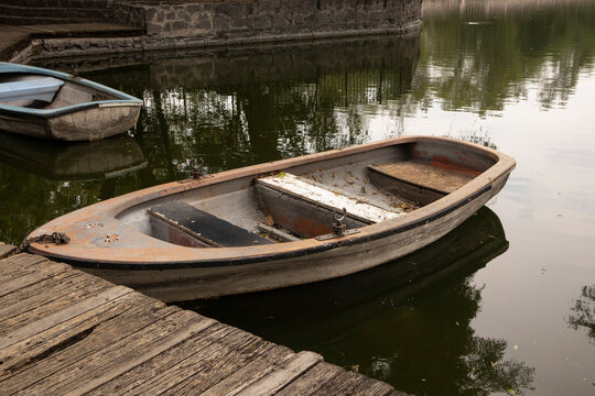 Rustic rowboat floating beside a wooden dock on calm reflective water in a peaceful lakeside setting