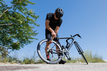 Fototapeta premium Bicycle repair on a sunny road with a cyclist fixing a flat tire during the day