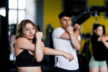 Fototapeta premium Fitness class in gym focused on stretching exercise with three participants in athletic clothing during afternoon workout session
