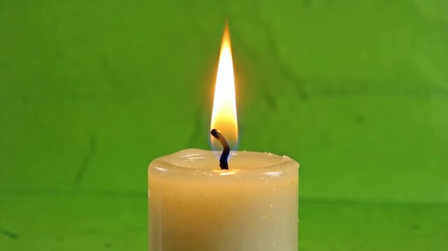 Burning candle with a steady yellow flame on green background