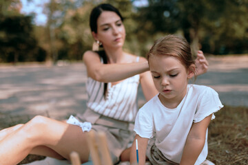 Fototapeta premium Mother Fixing Her Daughter's Hair During a Casual Outdoor Activity on a Sunny Day