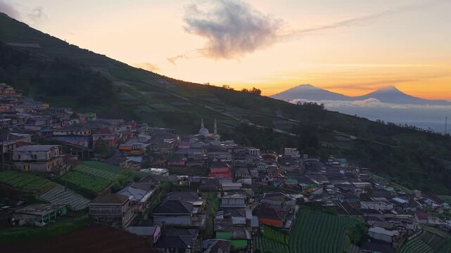 Golden sunrise aerial of hillside village, warm light over terraced farms and mountain landscape, peaceful rural homes and scenic countryside view Nepal Van Java, Indonesia.