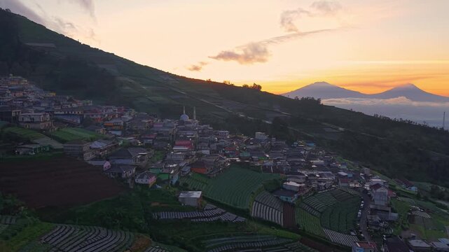 Aerial sunrise view of a mountain hillside village with dramatic sky and rural landscape. Serene countryside scenery with morning light and clouds. Nepal Van Java, Indonesia.