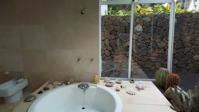 View of round bathtub decorated with large window facing volcanic rock wall in Haria, Lanzarote, Spain