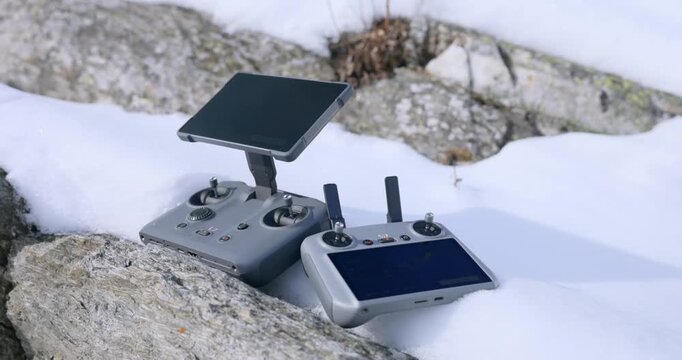 Drone controllers resting on snow and rocky terrain during an outdoor winter adventure