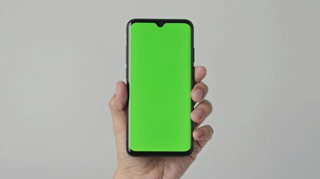 Hand holding a smartphone with a green screen for custom content