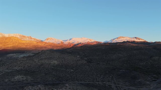 Beautiful golden hour light hitting the snowy Andes. Aerial view over the arid volcanic terrain in La Payunia Reserve, South America.
