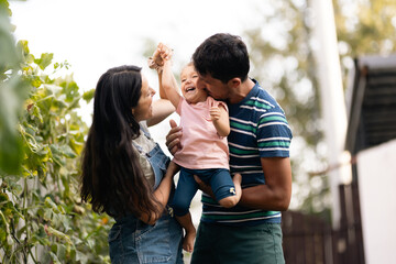 Fototapeta premium Loving Parents Holding Their Child Outdoors in a Garden Setting on a Beautiful Day