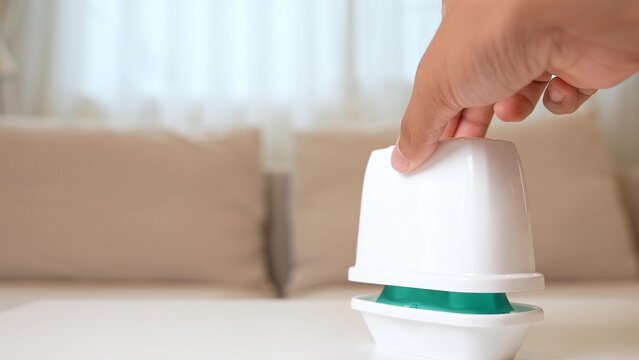 Lifting the lid of a gel air freshener at home represents caring for air quality, enhancing mood, daily cleanliness, easy maintenance, and creating a welcoming, comfortable atmosphere.
