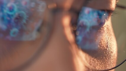 Fototapeta premium A person wearing glasses works on a laptop, with glowing reflections of viruses or bacteria in the lenses, symbolizing research, technology, health and broader conceptual ideas of science and society.