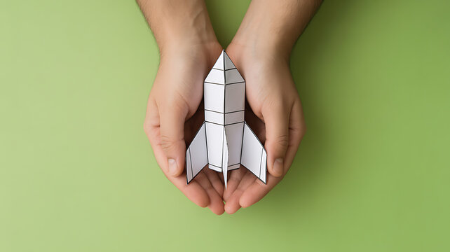 Person's hands holding a white paper rocket on a green background