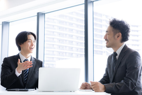 ノートパソコンを使いながら打ち合わせを行うビジネスマン二人　若手が提案する明るい営業シーン