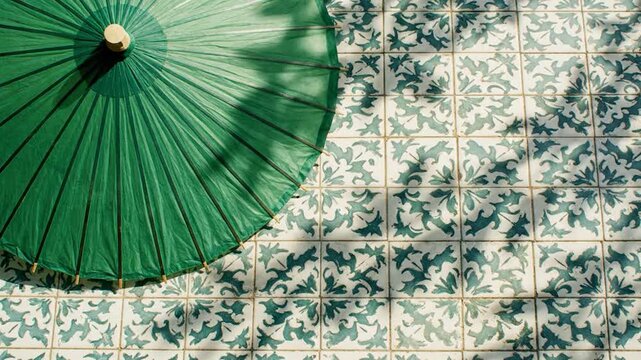 Green traditional paper umbrella resting on blue and white floral patterned tiles with sunlight and shadows
