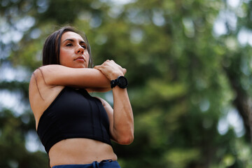 Naklejka premium Young woman in athletic wear stretching arms outdoors in a natural green environment