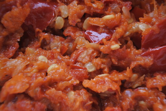 Macro texture of Indonesian sambal terasi, a traditional hot and spicy chili paste with shrimp paste, showing crushed red chili peppers and seeds.