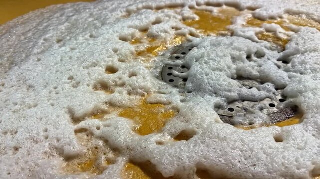 Close up view of static soapy suds and bubbles on textured yellow coating with steel grid plate