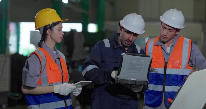 Technicians review machine operation with a rugged laptop at a production control station in a manufacturing facility, showing teamwork, monitoring, and process coordination.
