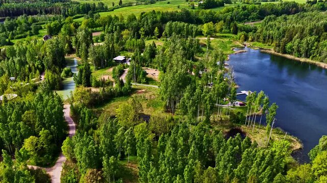 Birds-eye view flying over a serene lake, verdant forest, and a vacation resort with cottages