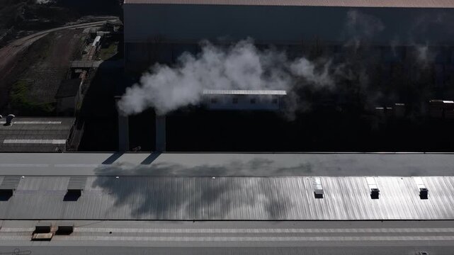 Static Aerial Drone Shot of Two Factory Chimneys Releasing Dense Smoke Over Industrial Rooftops in Piacenza Emilia Romagna Portraying the Heavy Toll of Industrial Pollution in Northern Italy