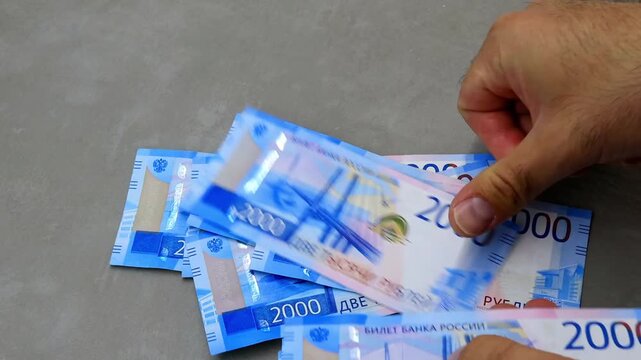 Male hand count blue cash Russia ruble stack on gray table to represent wealth for finance economy payment and business income