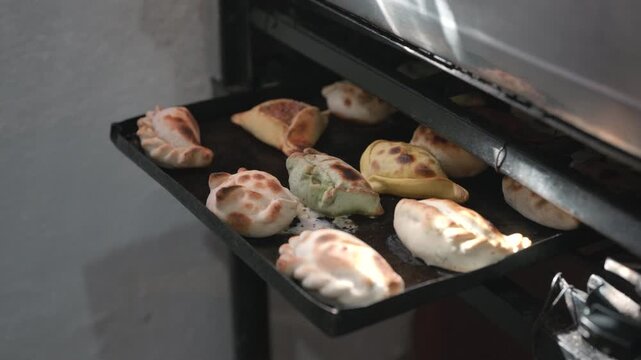 Traditional Argentine empanadas baking in oven on metal tray, featuring handmade folded pastry shapes, colorful dough varieties and artisanal culinary preparation, slow motiom arch shot reveal