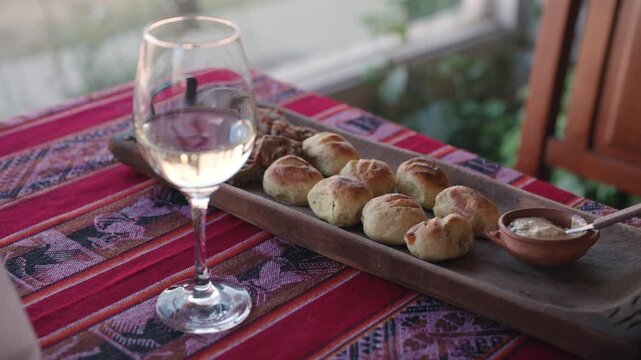 Rustic dining table with baked bread, white wine and delicatessen appetizers served beside creamy dipping sauce, featuring artisanal cuisine presentation and warm natural light, slow reveal arc shot.
