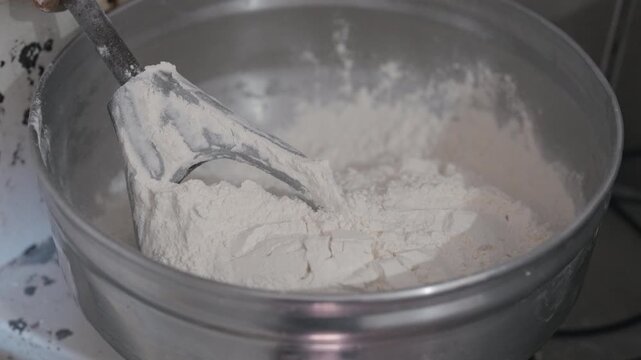 Wheat flour inside metal preparation bowl with mixing paddle during artisanal dough production, featuring small batch bakery workflow and handcrafted culinary preparation, closeup kitchen shot.