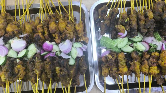 Freshly grilled chicken and beef satay sticks served neatly inside a takeout box. The delicious skewered meat is arranged perfectly on a table, ready to eat.