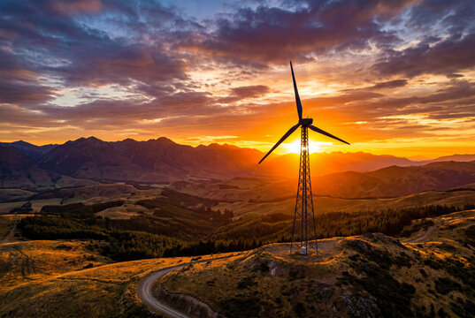 Large wind turbine standing on mountain peak during dramatic golden hour sunset