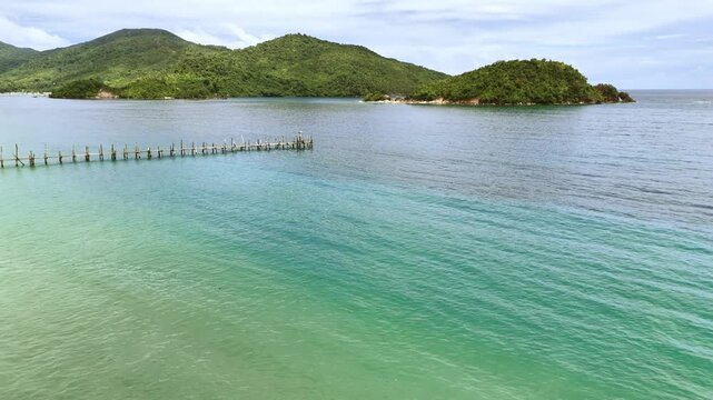 Push-in drone shot flying above a tropical shoreline in Palawan, Philippines, moving past rows of coconut trees and a long wooden dock extending over turquoise waters