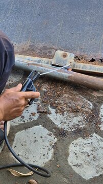 Worker Welding Metal Hinge Bracket on Heavily Rusted Iron Gate Frame Using Stick Welder