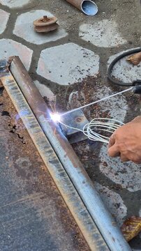 Worker Welding Metal Hinge Bracket on Heavily Rusted Iron Gate Frame Using Stick Welder