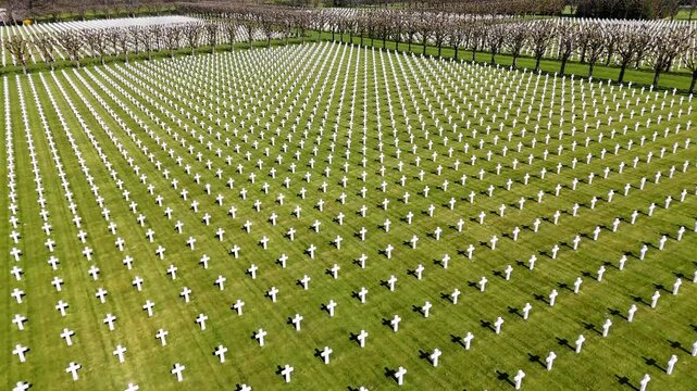 Drone view of white grave crosses in orderly rows on green lawn at Meuse-Argonne American Cemetery and Memorial in France.