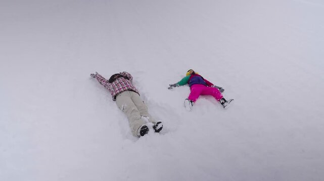 A playful mother and child lying in fresh winter snow making fun snow angels together.